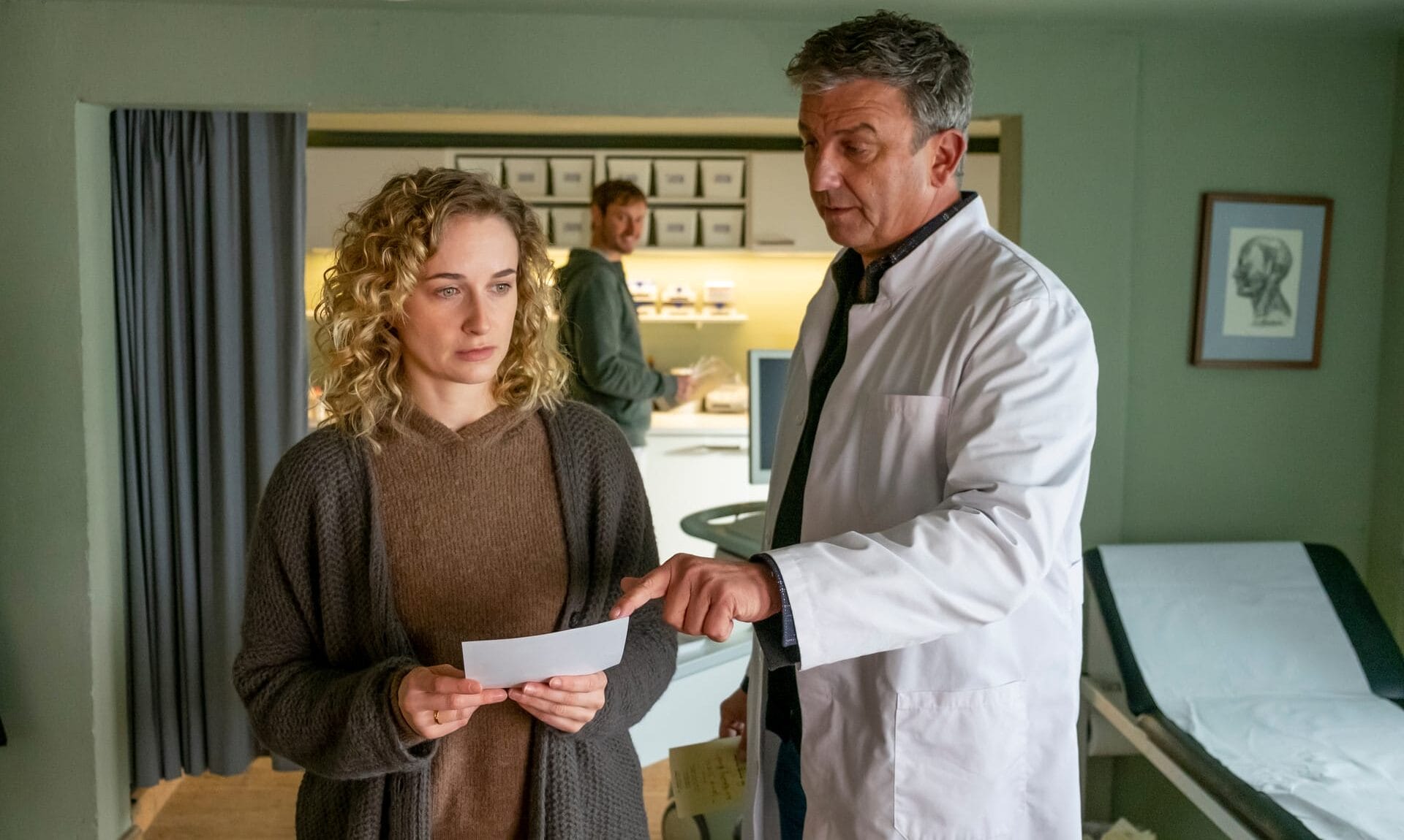 Dr. Martin Gruber (Hans Sigl, r.) hat für seine Patientin Jana Weiss (Pia Barucki, l.) gute Nachrichten: Sie ist schwanger. Doch ihre Freude ist verhalten, was auch David Ka?stner (Fre?de?ric Brossier, M.) irritiert.